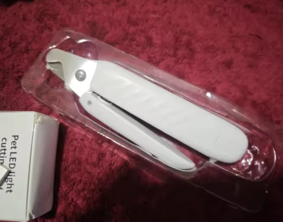 Customer photo of the LED Dog Nail Trimmer sealed in packaging on a red fabric surface
