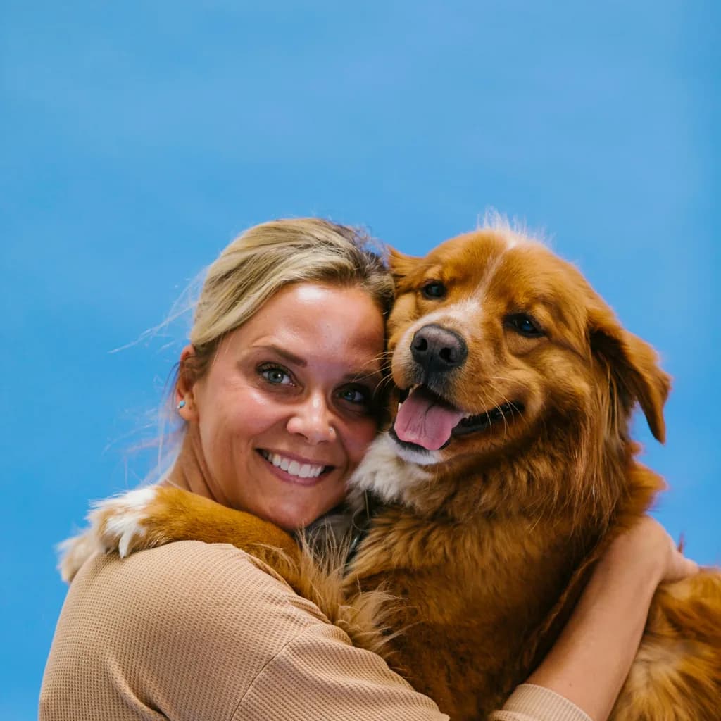 Smiling dog owner holding her happy dog against a blue backdrop